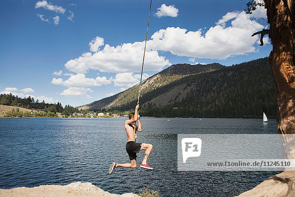 Junger Mann schwingt auf Seilschaukel über dem See,  Mammoth Lakes,  Kalifornien,  USA