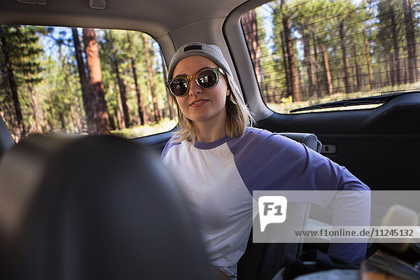 Porträt einer jungen Frau mit Sonnenbrille auf dem Rücksitz eines Autos
