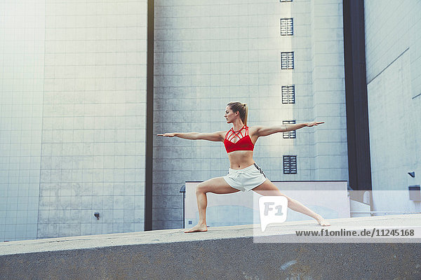 Junge Frau im Freien  in Yogastellung an der Wand stehend