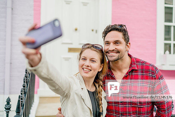 Young couple taking selfie in front of pink house  Kings Road  London  UK