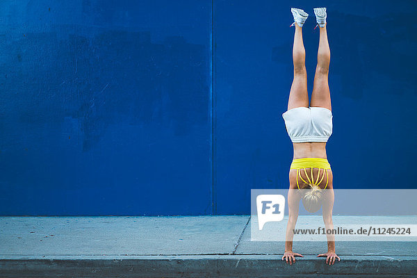 Junge Frau macht Handstand im Freien vor blauer Wand