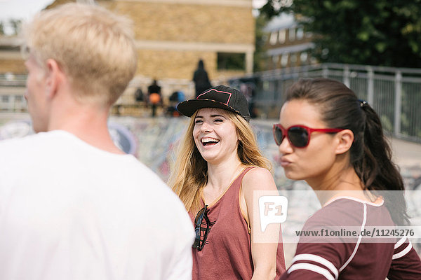 Three male and female friends laughing in city skatepark