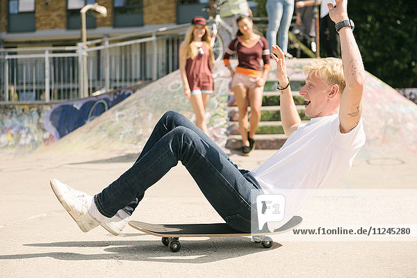Junger männlicher Skateboardfahrer sitzt auf einem Skateboard und bewegt sich im städtischen Skatepark