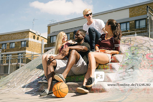 Vier männliche und weibliche Basketball-Freunde sitzen im städtischen Skatepark und unterhalten sich