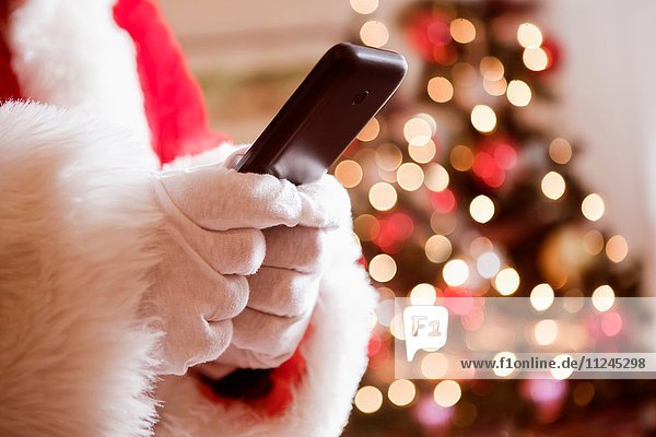 Geschnittene Ansicht eines Mannes im Weihnachtsmannkostüm  der ein Mobiltelefon hält