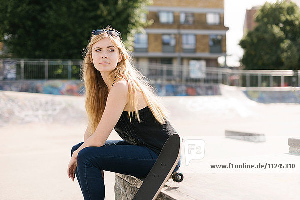 Porträt einer jungen Skateboarderin im Skatepark sitzend