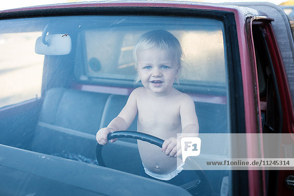 Porträt eines männlichen Kleinkindes  das im Lastwagen steht und ein Lenkrad hält