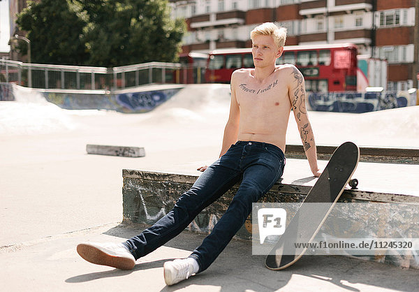 Tätowierter junger männlicher Skateboarder sitzt im Skatepark