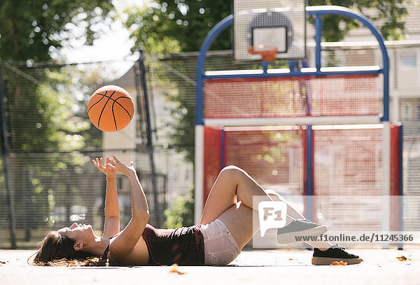 Junge Frau liegt auf Basketballfeld und wirft Ball