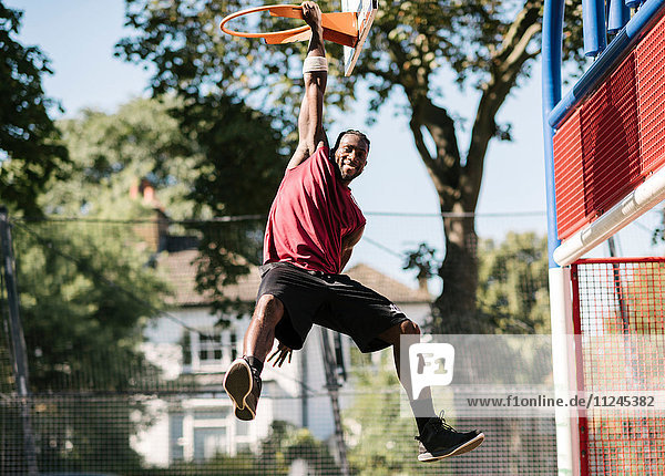 Porträt eines jungen männlichen Basketballspielers am Basketballkorb hängend
