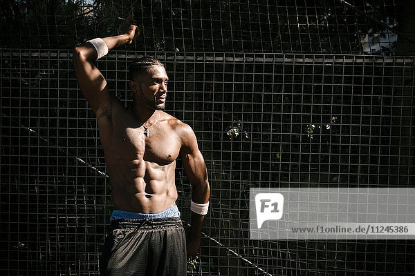 Bare-chested muscular young man posing by wire fence