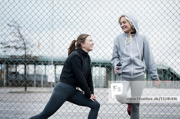 Two female running friends warming up by wire fence