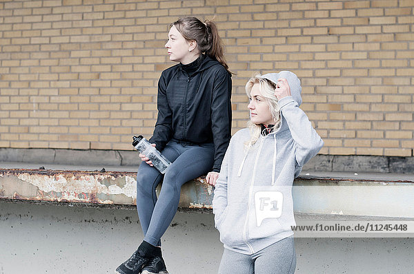 Two female running friends looking sideways outside warehouse