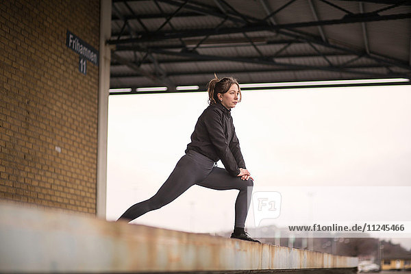 Female runner leaning forward stretching on warehouse platform
