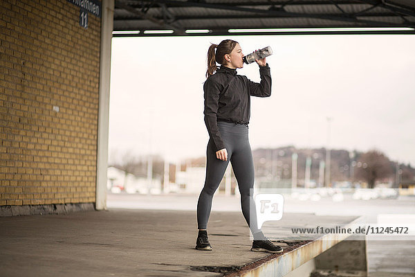 Weibliche Läuferin trinkt abgefülltes Wasser auf Lagerplattform