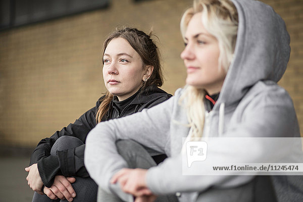 Two female runner friends sitting on warehouse platform