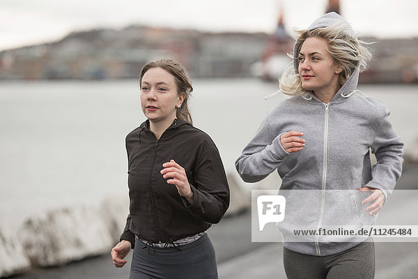 Two female runner friends running on dockside