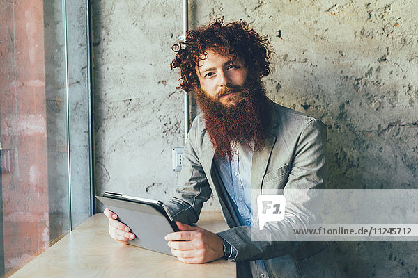 Porträt eines jungen männlichen Hipsters mit gelockten roten Haaren und Bart im Büro