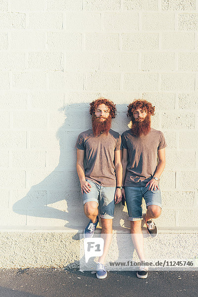 Porträt von eineiigen erwachsenen männlichen Zwillingen mit roten Haaren und Bärten an der weißen Wand.
