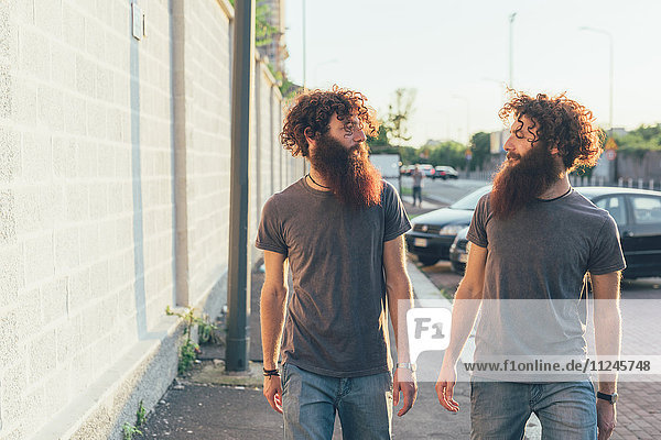 Eineiige erwachsene männliche Zwillinge  die auf dem Bürgersteig spazieren und plaudern