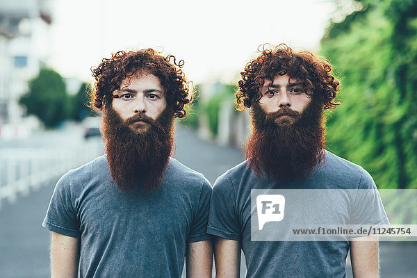 Porträt von eineiigen erwachsenen männlichen Zwillingen mit roten Haaren und Bärten auf dem Bürgersteig.