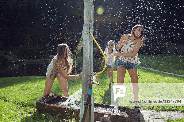 Drei erwachsene Freundinnen spielen im Garten mit dem Wasserschlauch