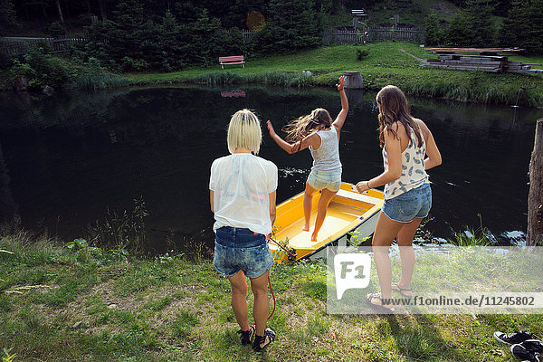 Three adult female friends jumping into rowing boat on lake  Sattelbergalm  Tirol  Austria