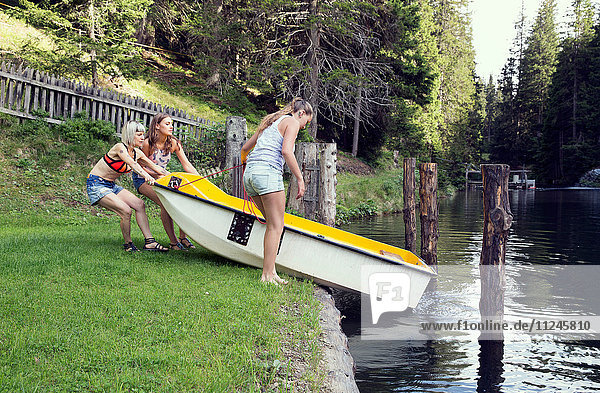 Drei erwachsene Freundinnen lassen Ruderboot in den See gleiten  Sattelbergalm  Tirol  Österreich