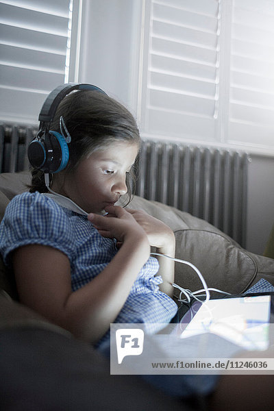 Schulmädchen sitzt auf dem Sofa mit einem digitalen Tablet und hört Kopfhörer