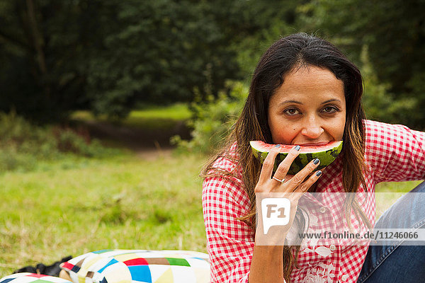 Porträt einer reifen Frau im Freien  die auf einem Feld sitzt und Wassermelone isst