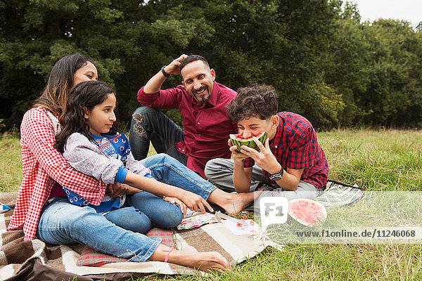 Familie sitzt im Freien  auf einer Picknickdecke  Sohn isst Wassermelone