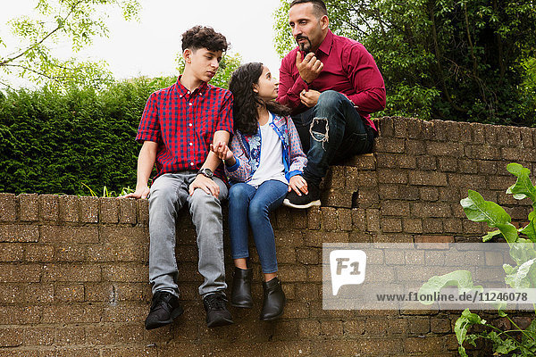 Vater sitzt mit Sohn und Tochter an der Wand