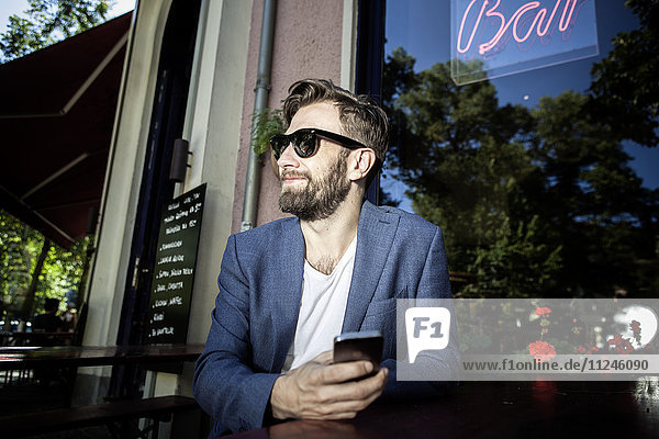Mann vor der Bar mit lächelndem Smartphone in der Hand,  Berlin,  Deutschland