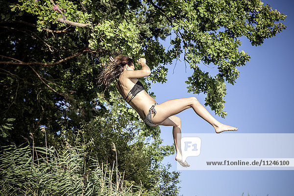 Frau im Bikini auf Baumschaukel schwimmend