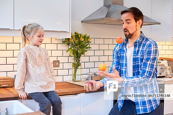 Mittelgroßer Mann jongliert in der Küche mit Obst für die Tochter