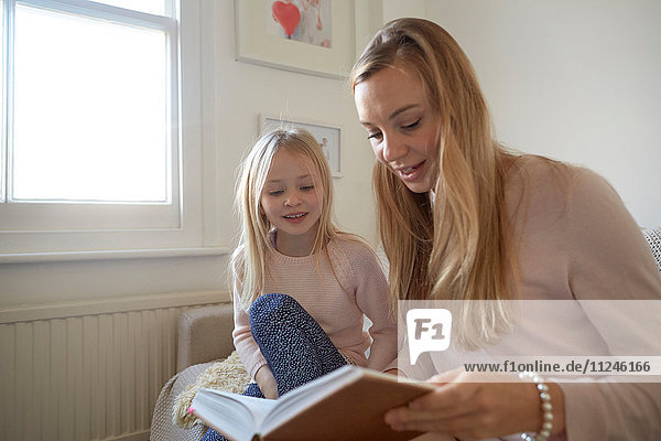 Mittlere erwachsene Frau liest der Tochter im Wohnzimmer vor
