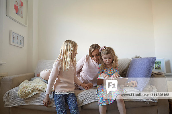 Mittlere erwachsene Frau und Töchter lesen Märchenbuch auf dem Sofa