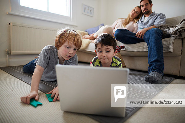 Brüder spielen Laptop-Spiel auf dem Zimmervorleger  Eltern auf dem Sofa