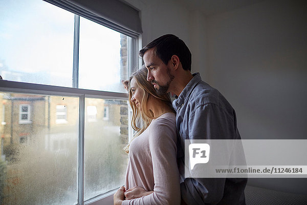 Mittleres erwachsenes Paar  das durch das Schlafzimmerfenster hinausblickt.