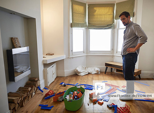 Mittelgroßer erwachsener Mann starrt auf im Wohnzimmer verstreutes Spielzeug