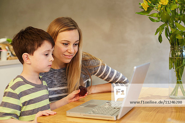 Mittelgroße erwachsene Frau und Sohn schauen auf den Laptop auf dem Esstisch