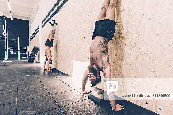 Two young male cross trainers doing handstands against gym wall