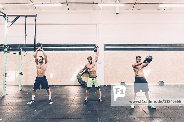 Three young male cross trainers training with kettlebells in gym