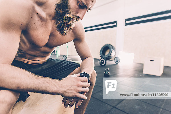 Young man sitting checking smartwatch in cross training gym