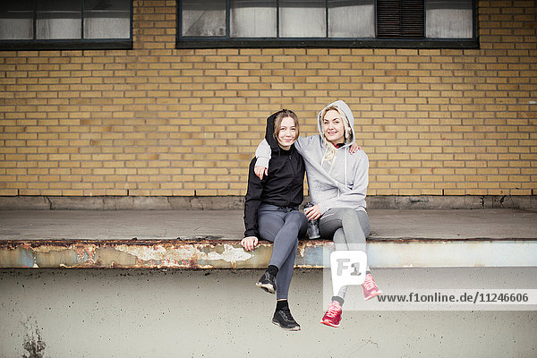Portrait of two female runner friends sitting on warehouse platform
