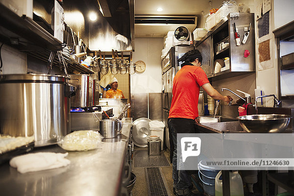 Der Ramen-Nudel-Laden. Ein Küchenchef  der in einer Küche arbeitet  in der das Essen mit einem Herd und großen Pfannen zubereitet wird.