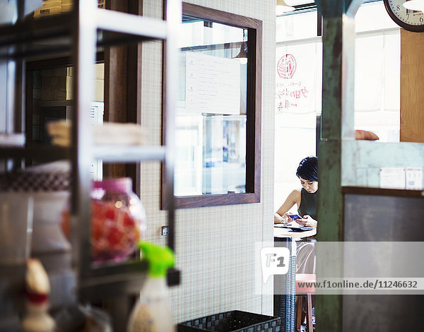 The ramen noodle shop. A woman sitting in a cafe view through a door.