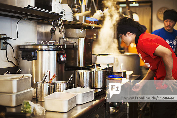 The ramen noodle shop. Staff preparing food in a tiny kitchen