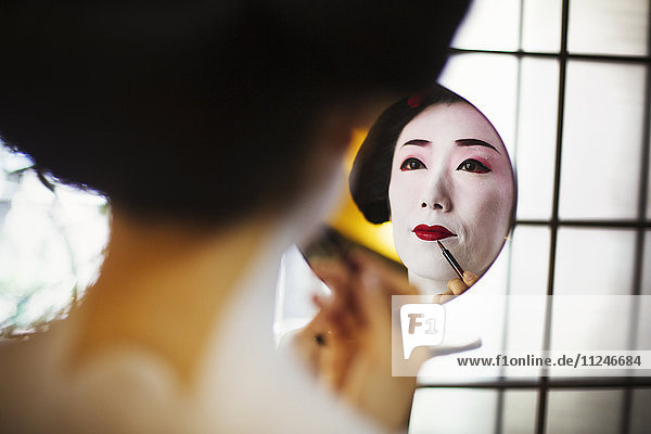 A modern geisha or maiko woman being prepared in traditional fashion  with white face makeup.
