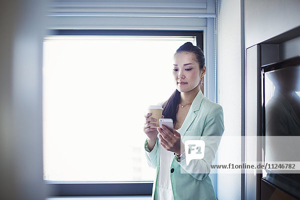 Eine Geschäftsfrau  die sich auf die Arbeit vorbereitet  eine Tasse Kaffee hält und ihr Smartphone kontrolliert.